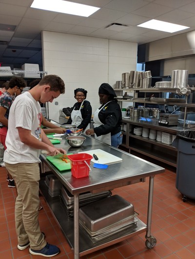 Black hats helping culinary arts students with knife skills.
