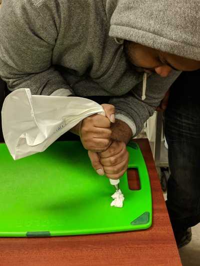 Male student creating his buttercream rose with white frosting.