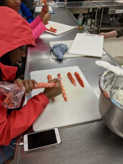 Female student creating a row of buttercream frosting roses with a rust colored frosting.  