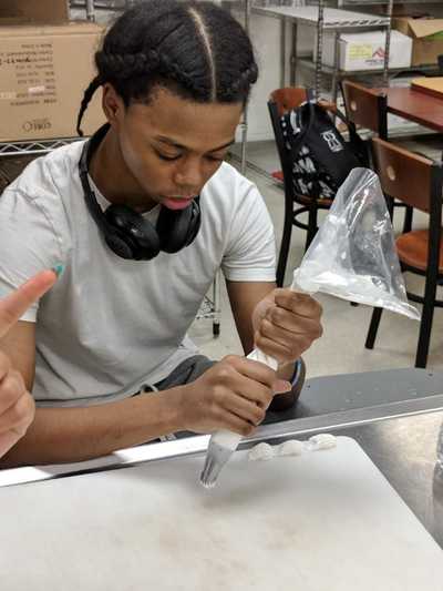 male student creating a row of buttercream frosting flowers.