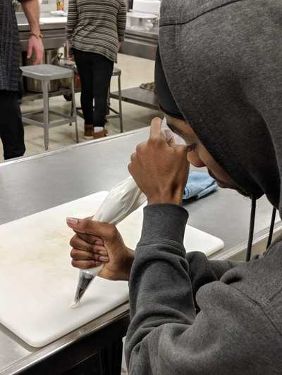 Male student squeezing pastry bag to create a buttercream frosting rose. 