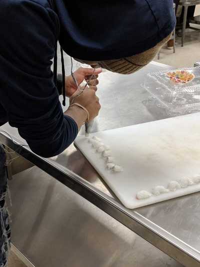Male student creating white buttercream frosting roses. 
