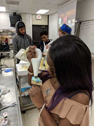 Female student creating a blue buttercream frosting rose.