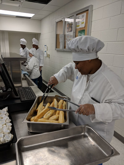 Student chef tossing breadsticks to serve.