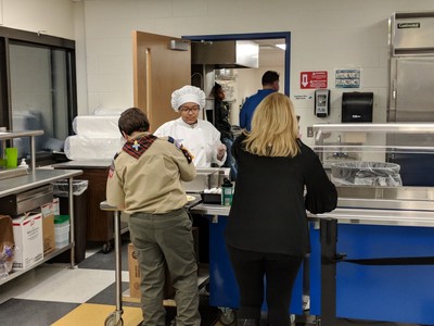Student chef serving patrons at event.
