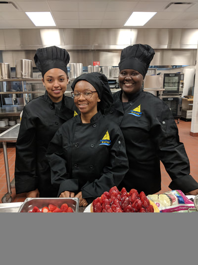 three second year student chefs referred to as black hats posing with strawberry cheesecake

