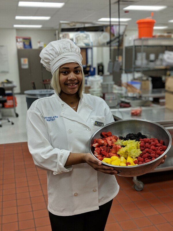 Student chef posting with fruit.