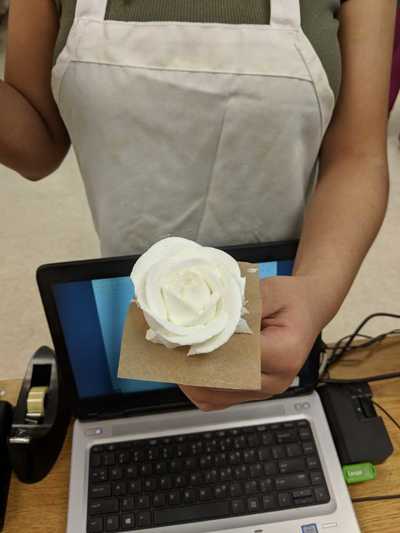Female student displaying her white buttercream frosting rose. 