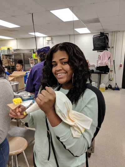 Female student smiling while displaying her yellow buttercream frosting rose.