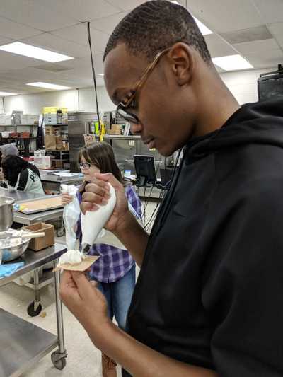 Male student creating his white buttercream frosting rose.  