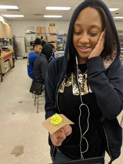 Female student smiling while displaying her yellow buttercream frosting rose.  