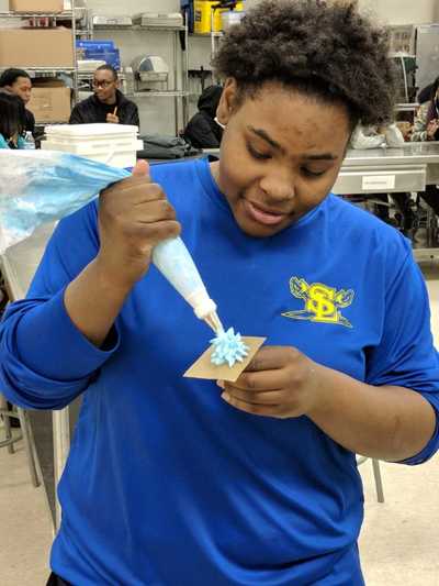 Female student smiling while creating her blue buttercream frosting rose.