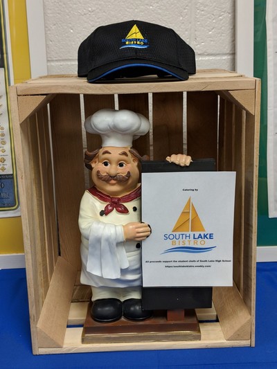 Chef statute in a wooden display crate with a black hat on top
