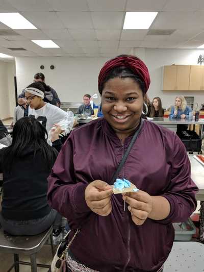Female student smiling while displaying her blue buttercream frosting rose.  