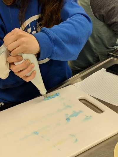 Female student practicing decorating techniques with blue buttercream frosting.