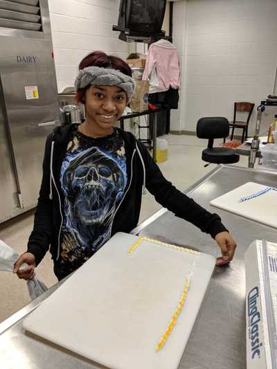Female student smiling while displaying her finished yellow and white buttercream frosting decorating.