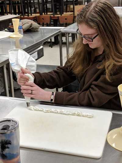 Female student using white buttercream frosting to decorate a cake.  