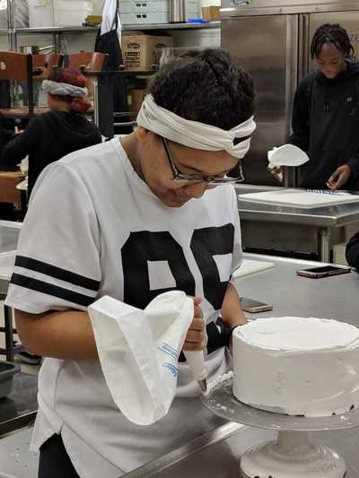 Female student decorating a styrofoam cake with buttercream frosting.