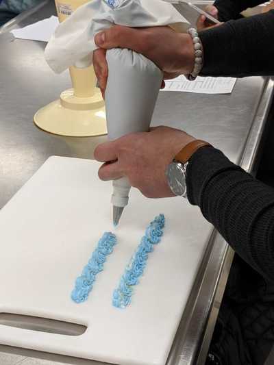 Male student using blue buttercream frosting to practice cake decorating practices.