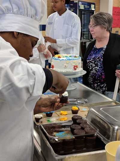 Student chef decorating brownie bite with frosting. 
