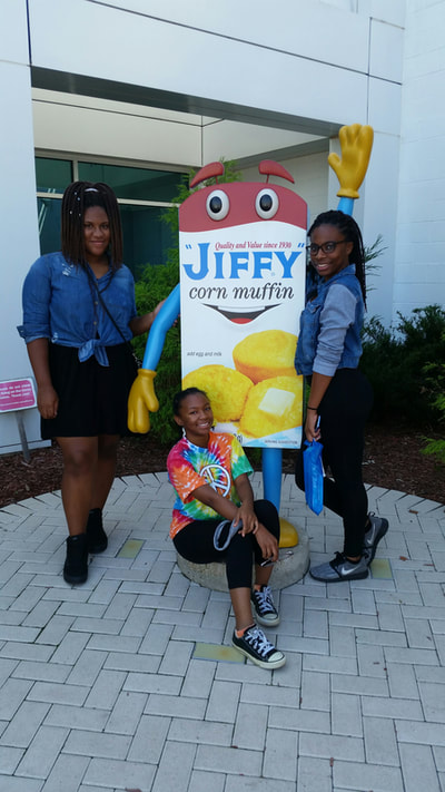 Students posing by Jiffy Mix box in front of building.