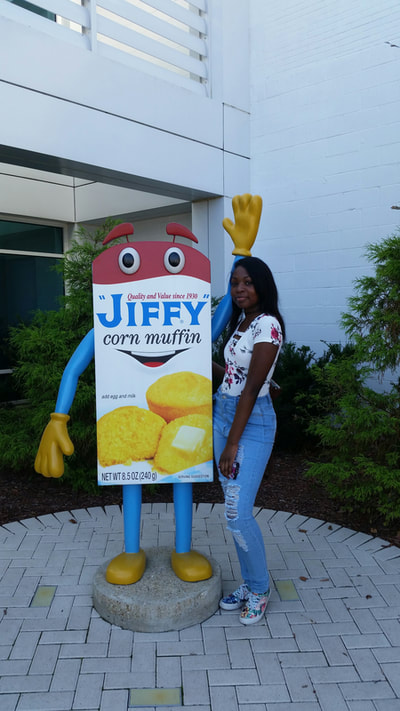Picture of student posing with Jiffy Mix box at front entrance.