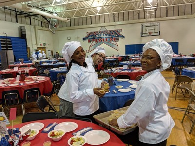 Student chefs smiling 
 and posting while passing out dressing for salads.