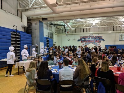 Picture of students coming up to be served their main course by student chefs.
