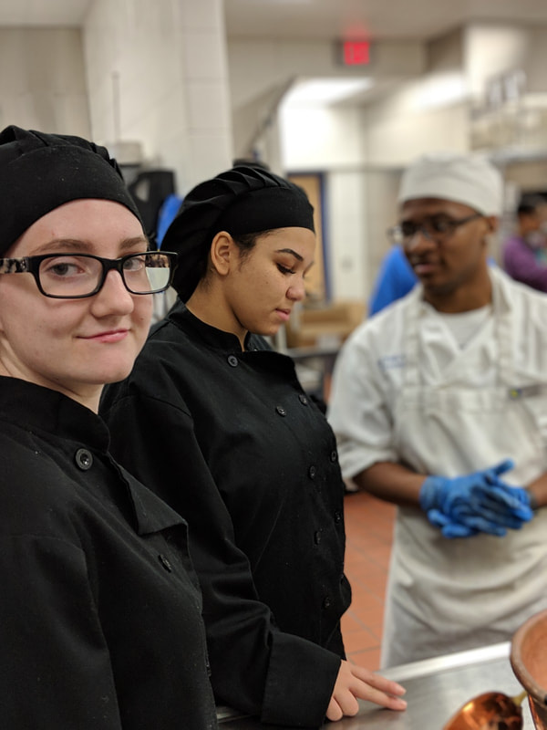 Black hat smiling with two other student chefs in background