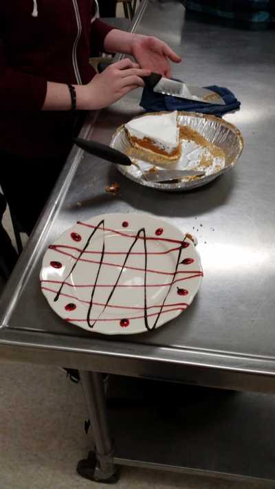 chocolate and strawberry syrup decorated plate in a zig zag fashion with a piece of pie off to the side