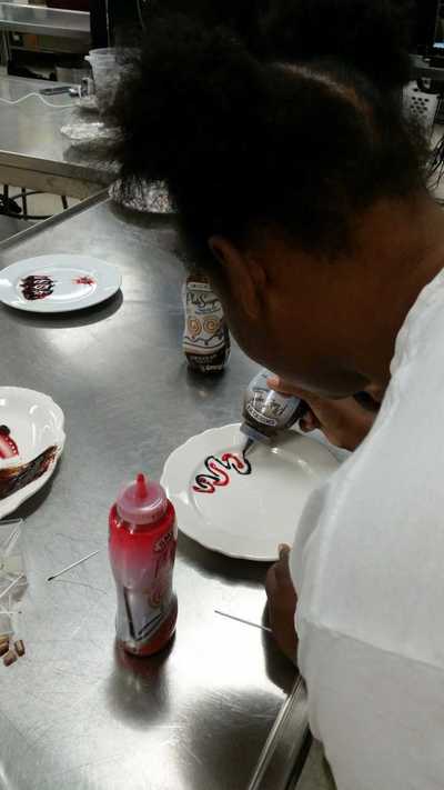 plate being decorated by student with chocolate and strawberry syrup in a squiggly pattern