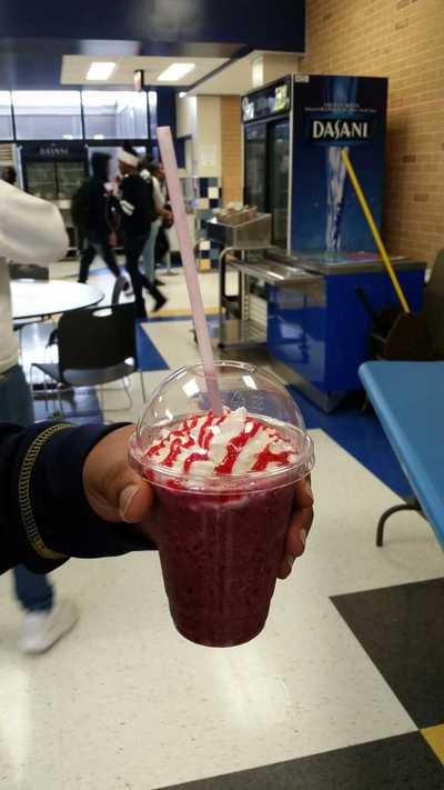 Picture of the Berry Blast smoothie iwith whipped cream and strawberry drizzle being held by a student.