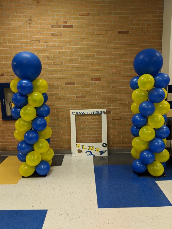 Photo area with blue and gold balloons and picture frame to pose with